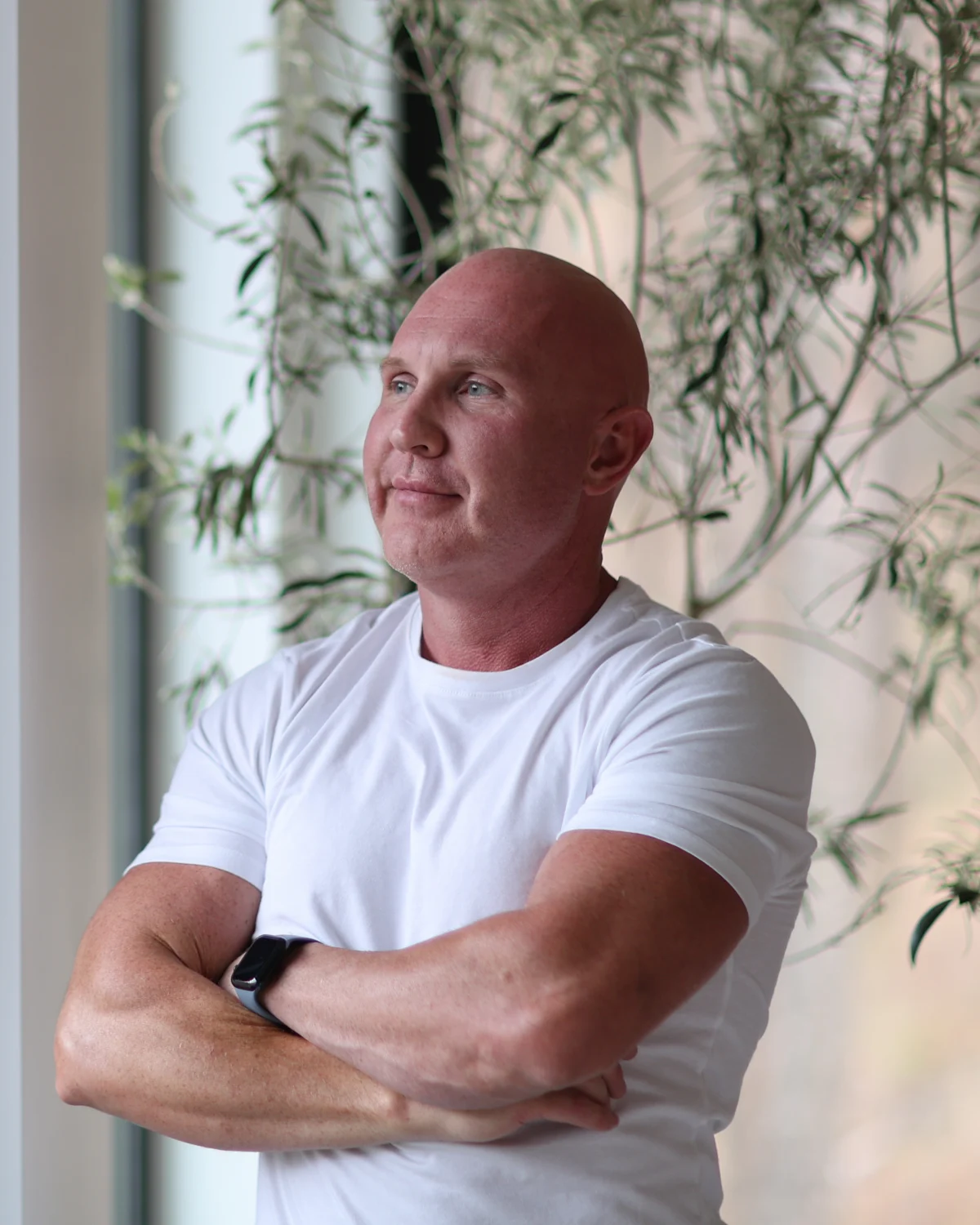 Dr. Kaleb Falk standing in a white T-shirt with his arms crossed beside a patio door.