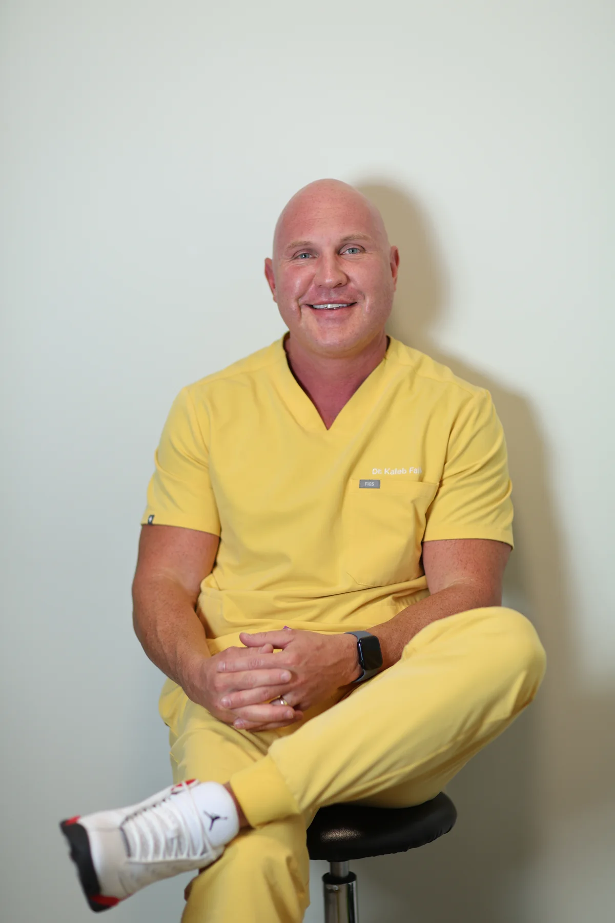 Dr. Kaleb Falk, ND, smiling while seated in pale yellow scrubs.